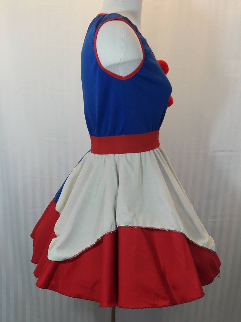 Puede incluir: Un vestido azul y rojo con una falda blanca. El vestido tiene un ribete rojo alrededor del escote y una cintura roja. La falda tiene una capa blanca y una capa roja.