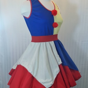 Puede incluir: Un vestido sin mangas rojo, blanco y azul con falda de c&iacute;rculo. El vestido tiene un corpi&ntilde;o amarillo y azul con ribetes rojos y pompones rojos.