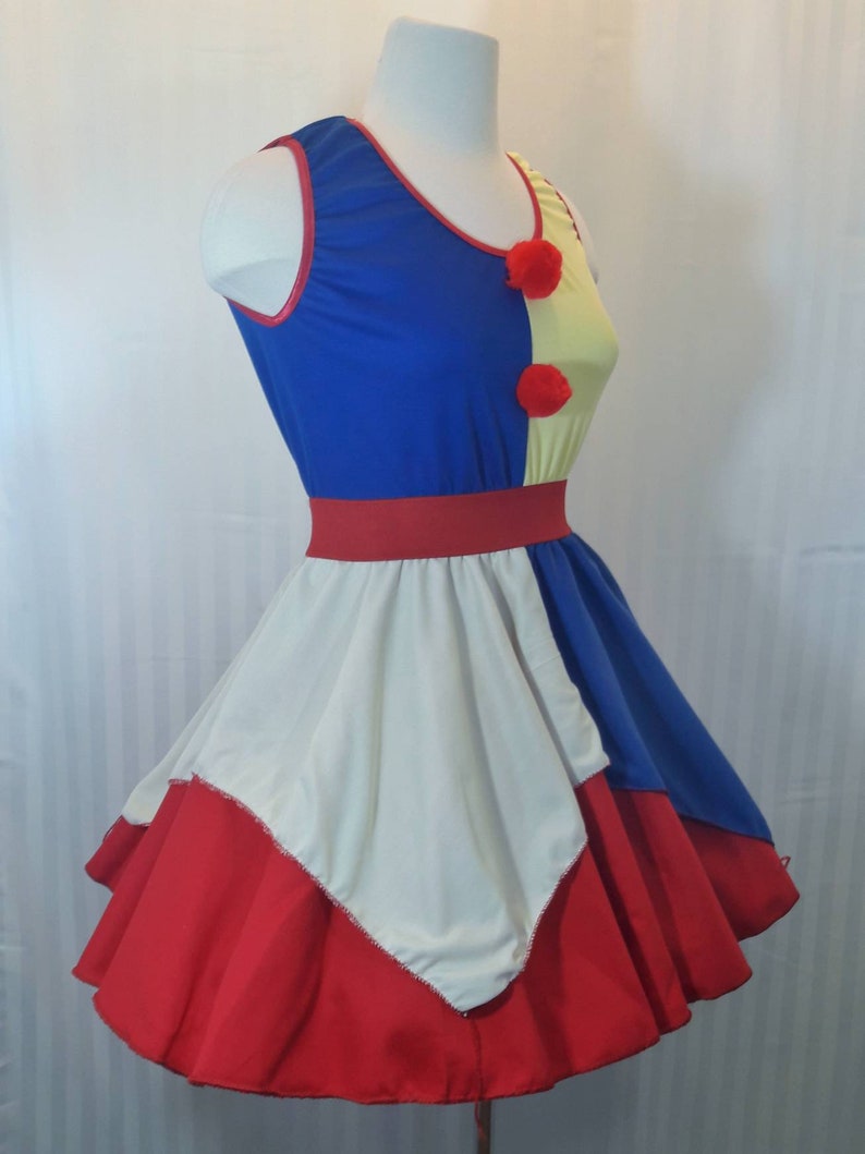 Puede incluir: Un vestido sin mangas rojo, blanco y azul con falda de c&iacute;rculo. El vestido tiene un corpi&ntilde;o amarillo y azul con ribetes rojos y pompones rojos.