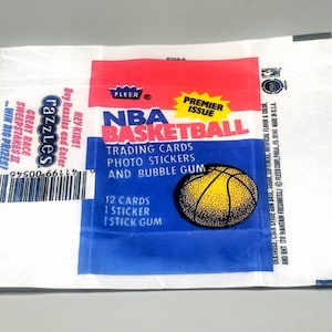 Puede incluir: Un paquete de cartas coleccionables de baloncesto de la NBA vintage con un gráfico de baloncesto amarillo. El paquete presenta el texto "Premier Issue" y "Trading Cards, Photo Stickers, and Bubble Gum". El paquete también tiene el texto "Razzles".