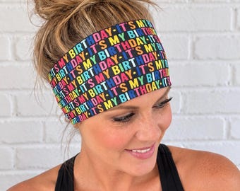 Puede incluir: Una diadema ancha de tela con fondo negro y el texto repetido IT'S MY BIRTHDAY impreso en letras vibrantes y multicolores que incluyen amarillo, rosa, azul y verde, acentuado con pequeñas estrellas amarillas entre frases.