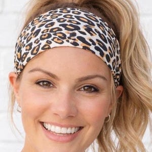 May include: A leopard print headband in black, brown, and cream. The wide headband is worn across the forehead. The accessory is made of a soft, stretchy material. Suitable for various activities, it measures approximately 5 cm in width.