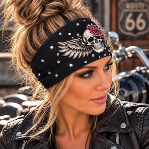 May include: A black headband featuring a graphic print of a skull with wings and a red rose on the side. The fabric is embellished with numerous small, clear, reflective rhinestones scattered across the surface of the black material.