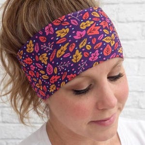 Può includere: Una fascia viola con un motivo a foglie colorate nelle tonalità dell'arancione, del rosa e del giallo. La fascia è indossata sulla fronte ed è realizzata in un tessuto morbido ed elastico. Il design presenta varie forme di foglie.