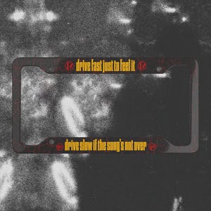 Peut inclure: Cadre de plaque d'immatriculation noir avec des accents rouges fissurés et du texte doré. Le texte supérieur indique "drive fast just to feel it" et le texte inférieur indique "drive slow if the song's not over".