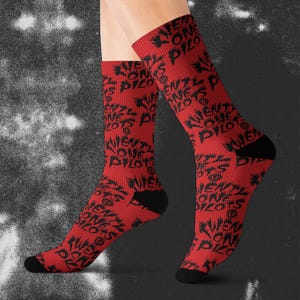 May include: Red socks with black text that reads "TWENTY ONE PILOTS" in a repeating pattern. The socks have black heels and toes. The socks are knee-high.