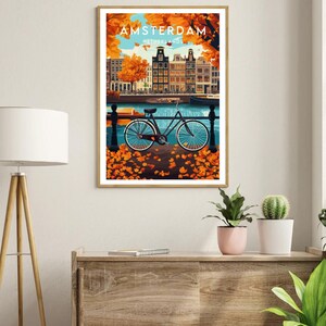 May include: A vintage travel poster featuring a bicycle parked in front of a canal in Amsterdam, Netherlands. The poster has a blue, green, and orange color scheme with fall foliage in the foreground.