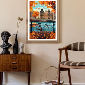 May include: A vintage travel poster featuring a colorful illustration of Amsterdam, Netherlands. The poster depicts a bicycle parked on a cobblestone street with a canal and buildings in the background. The text "AMSTERDAM, NETHERLANDS" is printed on the poster.