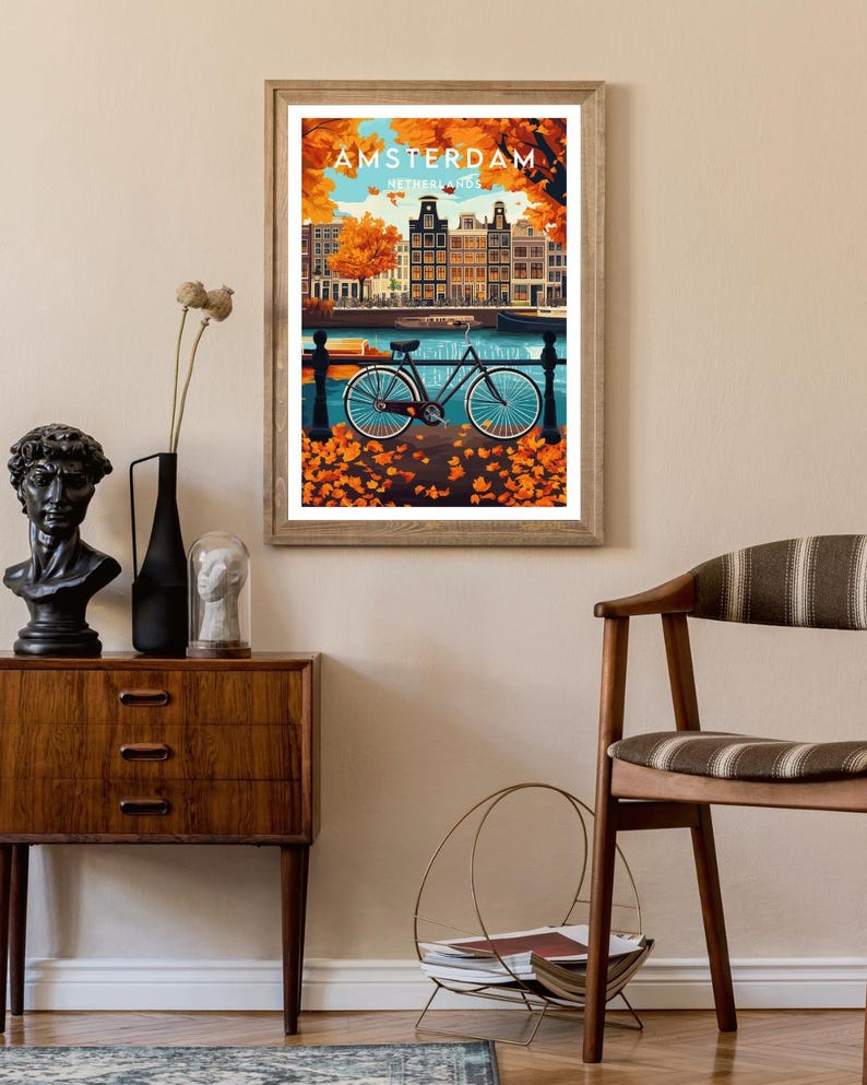 May include: A vintage travel poster featuring a colorful illustration of Amsterdam, Netherlands. The poster depicts a bicycle parked on a cobblestone street with a canal and buildings in the background. The text "AMSTERDAM, NETHERLANDS" is printed on the poster.