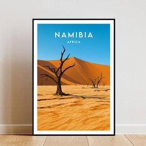 May include: Framed art print depicting a Namibian desert scene. The image shows a clear blue sky, orange sand dunes, and bare trees. The word "NAMIBIA" is printed at the top, with "AFRICA" below it.