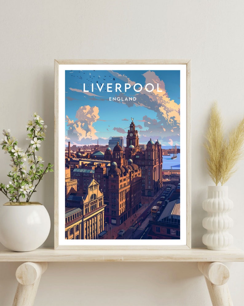 May include: A framed art print featuring a stylized illustration of Liverpool, England. The artwork depicts a cityscape with detailed buildings under a blue sky with clouds. The word "LIVERPOOL" is at the top, with "ENGLAND" below it.