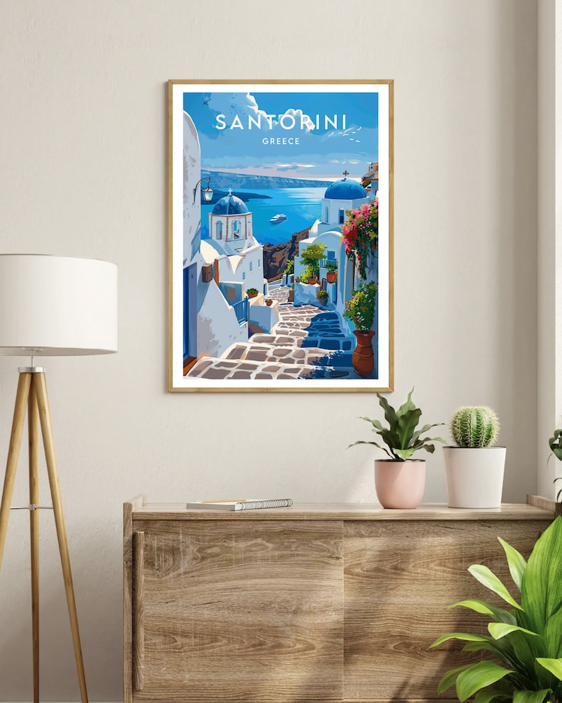 K&ouml;nnte beinhalten: Ein Vintage-Reiseposter mit einer blauen und wei&szlig;en Illustration einer Stra&szlig;e in Santorini, Griechenland. Das Poster zeigt eine blaue Kuppelkirche, wei&szlig;e Geb&auml;ude und eine gepflasterte Stra&szlig;e, die hinunter zum blauen &Auml;g&auml;ischen Meer f&uuml;hrt. Der Text "SANTORINI GRIECHENLAND" steht oben auf dem Poster.