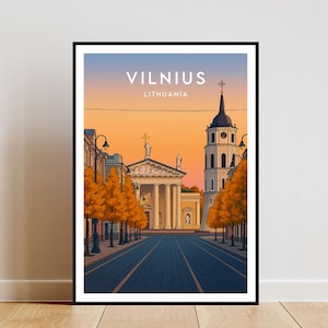 Puede incluir: Impresión artística enmarcada de Vilna, Lituania, que representa una escena callejera con una catedral y un campanario. El cielo hace la transición de azul a naranja. La impresión se exhibe en una pared blanca sobre un suelo de madera.