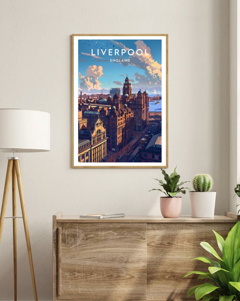 May include: A framed art print featuring a stylized illustration of Liverpool, England. The artwork showcases a cityscape with prominent buildings under a blue sky with clouds. The print is in a wooden frame and displayed on a wooden cabinet.