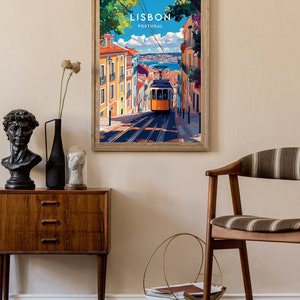 May include: A framed vintage travel poster with a colorful illustration of a yellow tram traveling up a hill in Lisbon, Portugal. The poster has the text "LISBON PORTUGAL" at the top.