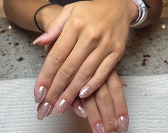 May include: Hands with long, oval-shaped, light pink nails. The nails have a pearlescent, shimmering finish. The hands are resting on a white towel.