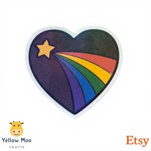 Pu&ograve; includere: Adesivo a forma di cuore con un design arcobaleno. L'adesivo presenta uno sfondo viola scuro con una stella gialla e un arcobaleno che ne emana. L'arcobaleno comprende i colori rosso, arancione, giallo, verde, blu e viola. L'adesivo ha un bordo bianco.