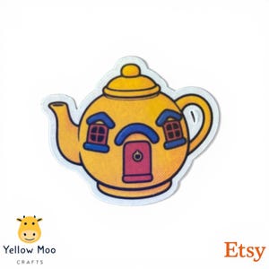 Pu&ograve; includere: Un adesivo a forma di teiera gialla con un design a casa. L'adesivo presenta un corpo giallo, un ingresso ad arco blu, una porta rossa e cornici blu. L'adesivo ha un bordo bianco e si trova su sfondo bianco.