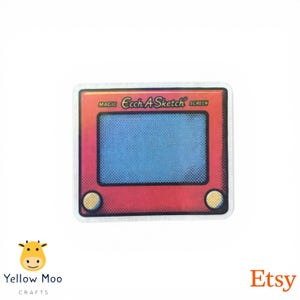 Pu&ograve; includere: Un adesivo rosso e rosa con un classico design Etch A Sketch con le parole "Magic Etch A Sketch Screen". L'adesivo ha un'area dello schermo blu e manopole gialle negli angoli inferiori. L'adesivo ha una forma quadrata.