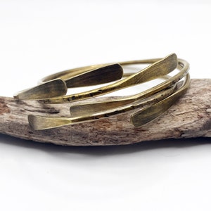 May include: A set of four brass bangles with a hammered texture. The bangles are stacked on top of each other and are arranged in a spiral pattern.