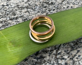 May include: Three gold rings stacked on top of each other. The rings are all different sizes and have a smooth, polished finish.