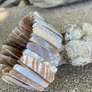 May include: A stretch bracelet made of iridescent, rectangular shell pieces. The bracelet features a mix of neutral colors, including cream, tan, and pearlescent white. The shell pieces are strung together, creating a flexible and textured accessory.