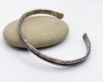 May include: A silver bracelet with a hammered texture and a slightly curved shape.