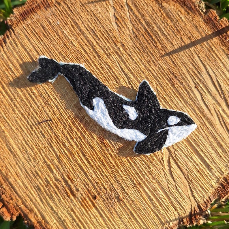 Pu&ograve; includere: Toppa ricamata di orca bianca e nera. L'orca sta nuotando verso destra. La toppa &egrave; su una superficie di legno.