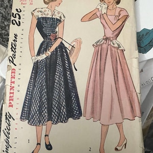 Könnte beinhalten: Vintage Simplicity Schnittmuster, Größe 12, Brustumfang 76 cm. Das Cover zeigt Illustrationen von zwei Kleidern: eines in blau-weißem Karomuster, das andere in Rosa. Der Text enthält "25c" und "Simplicity is America's Fashion."