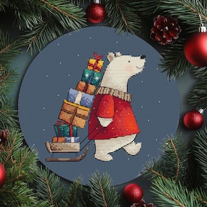 Könnte beinhalten: Ein Kreuzstichmuster eines Eisbären in einem roten Pullover, der einen Schlitten mit verpackten Geschenken zieht. Der Bär steht vor einem blauen Hintergrund mit Schneeflocken, umgeben von Weihnachtsschmuck und Tannenzweigen.