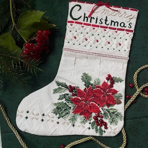 May include: White Christmas stocking with red and green embroidery of a poinsettia and holly. The stocking has a red ribbon and the words "Merry Christmas" embroidered on the top.