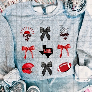 Pode incluir: Uma camisola cinzenta com designs de ferro em vermelho e preto. Os designs incluem um sol com as palavras "Suns Up", um laço, uma mão com as palavras "Guns Up", um contorno em forma de Texas com as letras "LBK", uma bola de futebol e um capacete.