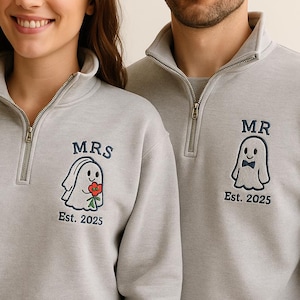 May include: Matching light gray sweatshirts with a quarter-zip collar. One sweatshirt has "MRS" embroidered above a ghost holding flowers, the other has "MR" above a ghost with a bow tie. Both have "Est. 2025".