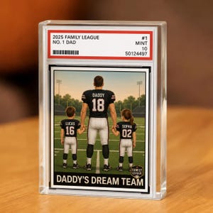 May include: A collectible trading card encased in a clear plastic slab featuring a football-themed illustration of one adult and two children standing on a field. The card text reads 2025 FAMILY LEAGUE, NO. 1 DAD, DADDY, LUCAS, SOPHA, and DADDY'S DREAM TEAM.