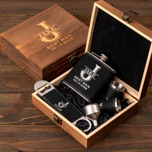 May include: A wooden gift set containing a personalized hip flask, shot glasses, and bottle opener. The black flask and opener feature white text: "Jake" and "Best Man 09-10-2028". The brown box has matching engraved text.