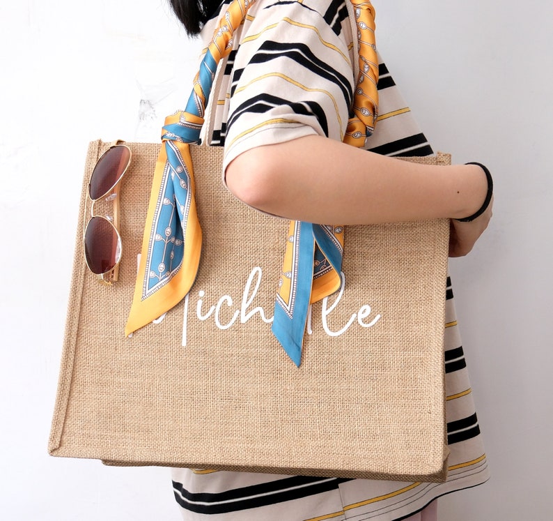 May include: A large, brown, burlap tote bag with a white inscription that reads "Michelle". The bag has a blue and yellow patterned scarf tied to the handles.