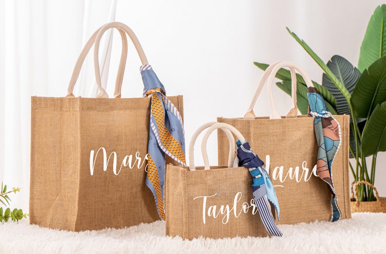 May include: Three brown burlap tote bags with white personalized names. The bags have white cotton handles and are decorated with colorful scarves.