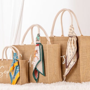 May include: Three brown burlap tote bags with white lettering and colorful patterned scarves. The bags are labeled "Sophie", "My", and "Sweet".