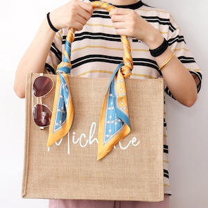 May include: A brown jute tote bag with a white inscription that reads "niche". The bag has a blue and yellow patterned scarf tied to the handles.