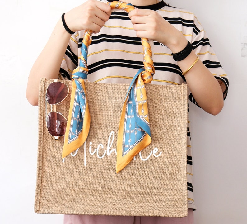 May include: A brown jute tote bag with a white inscription that reads "niche". The bag has a blue and yellow patterned scarf tied to the handles.