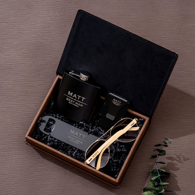 May include: A black gift box containing a flask, sunglasses, bottle opener, and a watch. The flask, bottle opener, and watch are engraved with the name "MATT" and "BEST MAN". The sunglasses have gold frames.
