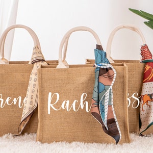 May include: Three brown burlap tote bags with white handles and personalized names: Brenda, Rachel, and Jess. Each bag has a colorful patterned scarf tied around the handle.