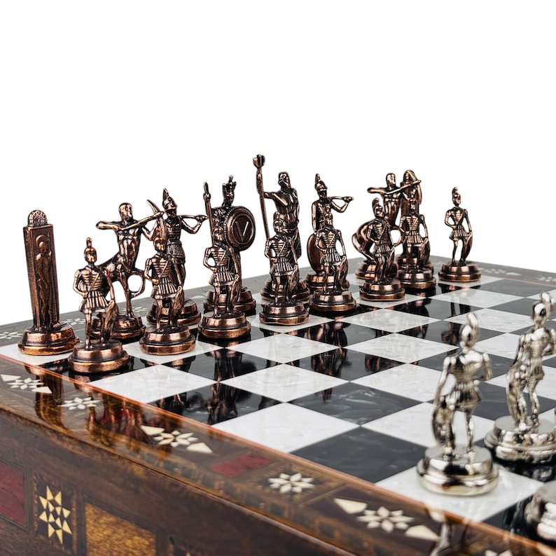May include: A chess set with bronze-colored pieces depicting ancient warriors. The board is black and white with a decorative wooden frame. The pieces are detailed and arranged on the board, ready for play.