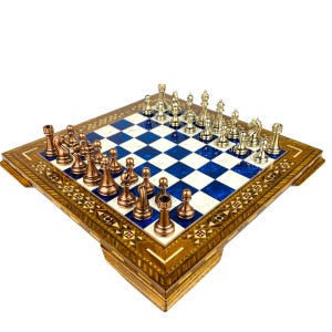 Könnte beinhalten: Ein Schachbrett aus Holz mit eingelegten Designs und blauen und weißen Feldern. Die Schachfiguren sind aus Metall, ein Satz in Kupfer und der andere in Silber.