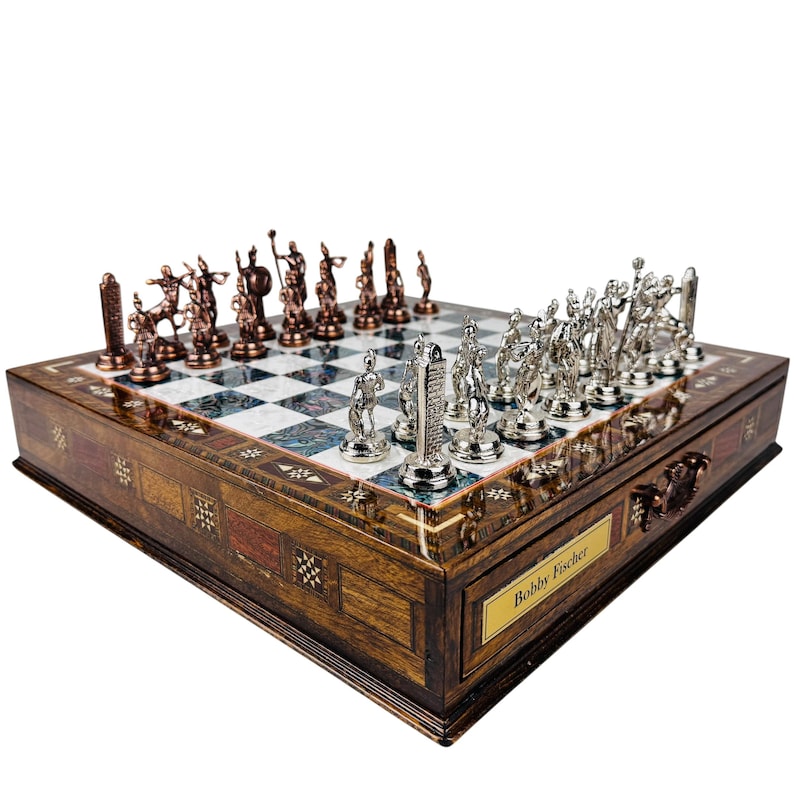 May include: A detailed chess set with bronze and silver pieces on a wooden board. The board has a checkered pattern with white and blue squares. The wooden box has a decorative inlay and a plaque that reads "Bobby Fischer."