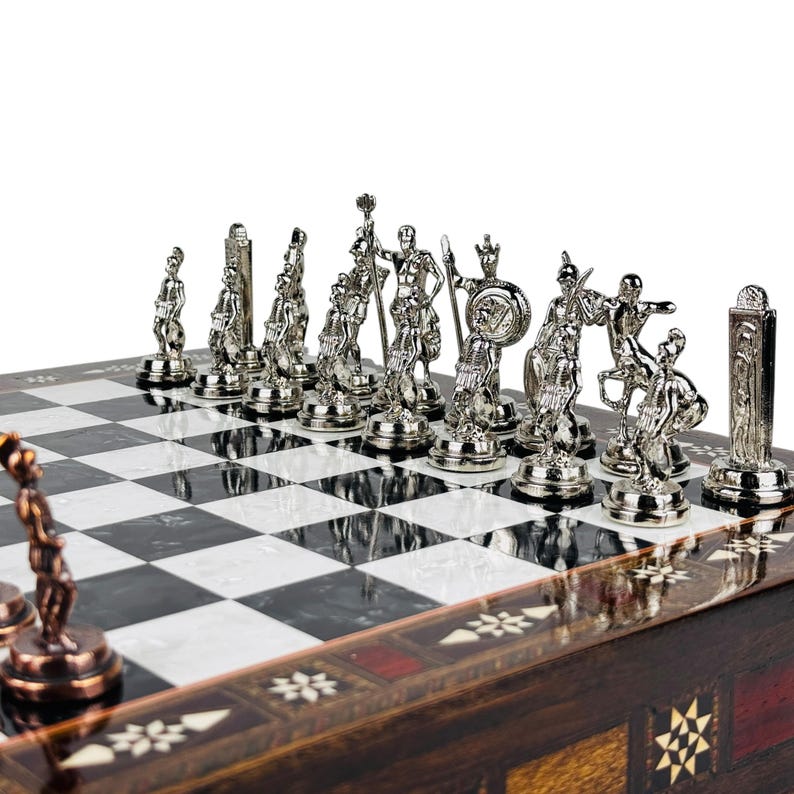 May include: A detailed chess set with silver-colored pieces depicting ancient warriors. The chessboard has a black and white checkered pattern, set on a wooden base with decorative inlays. The pieces are intricately designed.