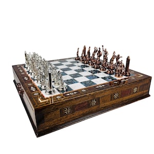 May include: A decorative chess set with a wooden board and ornate metal chess pieces. The board features a checkered pattern with a dark wood border. The chess pieces are silver and bronze, adding a touch of elegance to the game.
