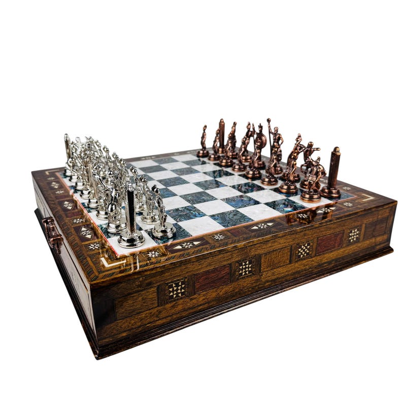May include: A decorative chess set with a wooden board and ornate metal chess pieces. The board features a checkered pattern with a dark wood border. The chess pieces are silver and bronze, adding a touch of elegance to the game.