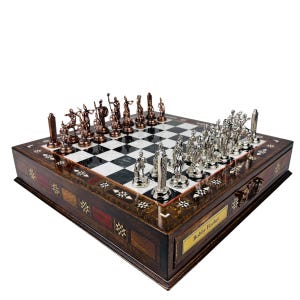 May include: A detailed chess set with bronze and silver pieces on a checkered board. The wooden box is inlaid with decorative patterns and features a drawer with a nameplate that reads "Bobby Fischer".