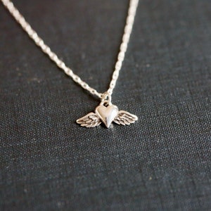 May include: A silver necklace with a heart pendant with wings. The heart is a simple design and the wings are small and delicate.